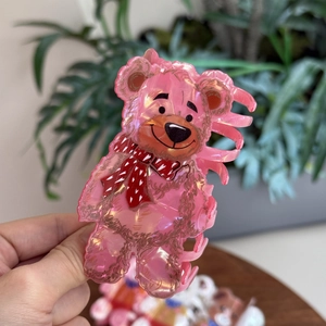 Detailed close-up of a pink acrylic teddy bear hair claw clip with polka dot scarf detail