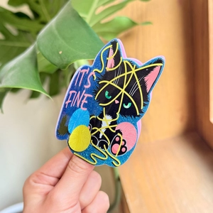 Macro shot of glittery black cat sticker entangled in colorful yarn with It's Fine text