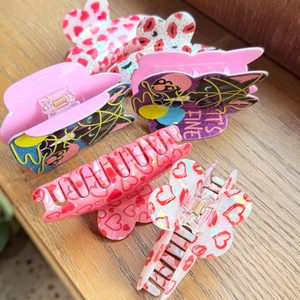 Close-up of acrylic hair claws with heart patterns and black cat design featuring It's Fine text