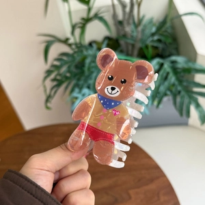 Detailed view of a cute brown acrylic bear hair claw clip held over a wooden background