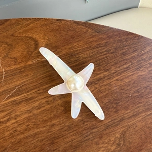 Barrette étoile de mer en acétate avec perle irisée sur une surface en bois