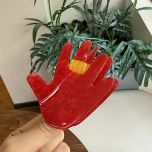 Macro shot of a red palm-shaped acrylic hair claw with yellow accent details