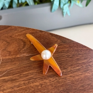 Barrette étoile de mer en acétate avec perle sur un socle en bois naturel