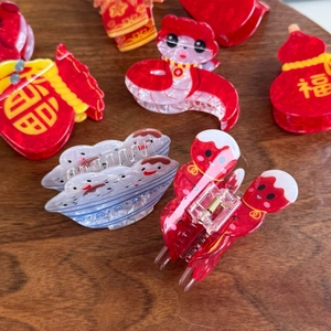 Close-up of Lunar New Year acrylic hair claws with festive red zodiac snake and fortune bag