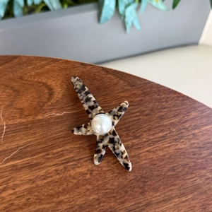Détail d'une pince à cheveux étoile de mer en acétate et perle sur bois sombre