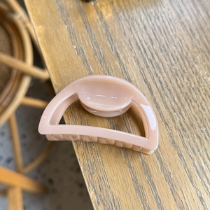 Macro detail of high-shine resin claw clip in soft pink on a wooden texture background