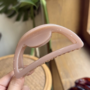 Close-up of pink hollow semicircular hair claw clip held over a rustic wooden background