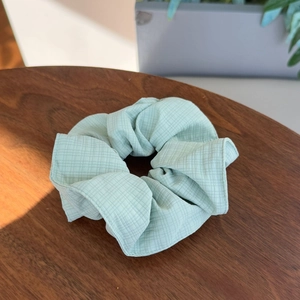 Plaid canvas hair scrunchie in mint green displayed on a rustic wooden table surface