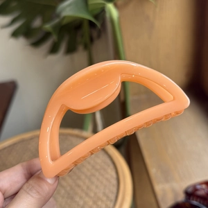 Macro detail of a 10cm peach orange hollow hair claw clip with smooth acrylic finish