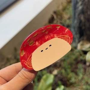 Handheld photo of a red mushroom acetate hair claw with gold dots and a smiley face design