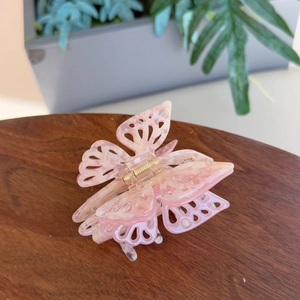 Pink butterfly hair claw clip with marble pattern and cutout design on wooden surface