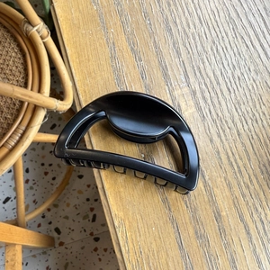 Minimalist black semi-circle hair claw clip with glossy finish on wooden table