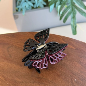 Detail of burgundy and black butterfly hair claw clip with cutout design on wood