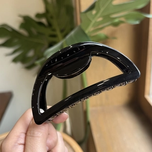 Detail showing hand holding a 10cm black glossy hollow hair claw clip in a cozy setting