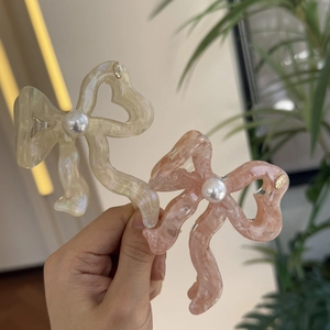 Detail of acetate bow hair claws in cream and pink marble with center pearl decoration