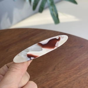 Détail d'une pince à cheveux ovale en acétate avec élégant motif marbré bordeaux et métal