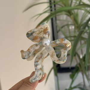 Detail of acetate bow hair claw with marble texture and large faux pearl accent