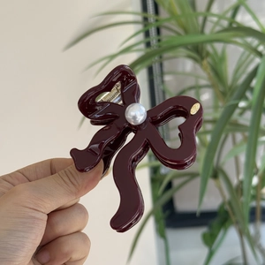 Close-up of a burgundy bow hair claw with elegant pearl detail and gold logo accent