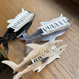 Three acetate shark hair claws in marble and monochrome patterns on a wooden surface