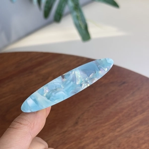 Pince à cheveux ovale en acétate avec texture marbrée bleu clair tenue en main