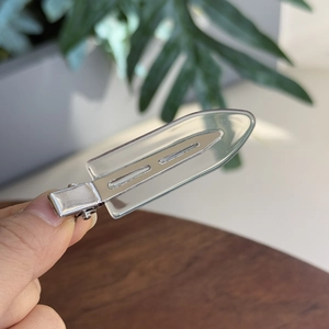Macro detail of a transparent resin hair clip with a silver metal duckbill base held in hand