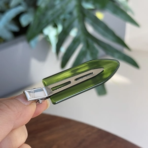 Close-up of a translucent green resin hair clip with a silver metal base in hand
