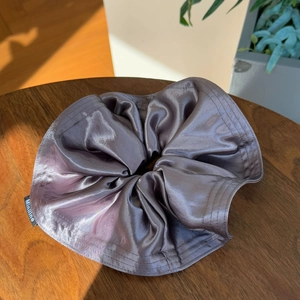 Close-up of a silver oversized satin scrunchie with pleated texture on a wooden table
