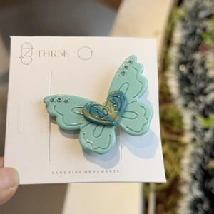 Elegant mint green butterfly hair clip with heart detail and blue rhinestones on card