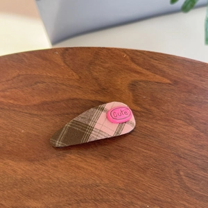 Pink and brown checkered hair clip with cute decorative button on a wooden table