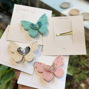 Detailed view of three butterfly hair clips in mint, cream, and pink with LOVE heart centers