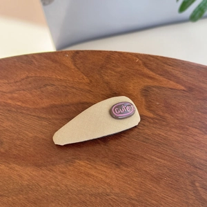 Detailed view of beige fabric snap hair clip with a brown cute tag on wood surface