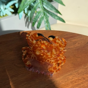 Tropical crab-shaped acetate hair claw clip with amber tortoise shell pattern on wood