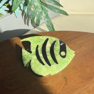Detail view of a pale green angelfish hair claw clip with marble texture on wood surface