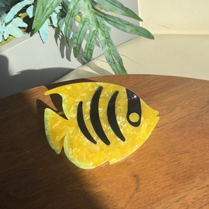 Detail of yellow acetate tropical fish hair claw clip with black stripes on wood surface