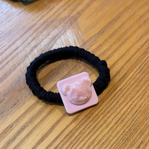 Detail of pink acrylic square charm with bear relief on black elastic hair rope