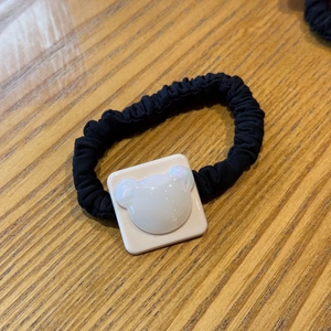 Close-up of a white pearlescent bear ornament on a black pleated elastic hair scrunchie