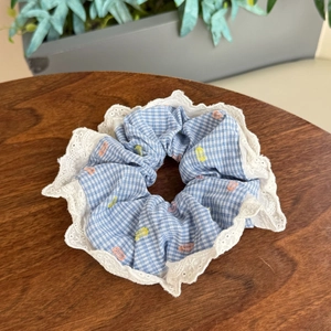 Close-up of blue plaid scrunchie with white lace trim and floral embroidery on wood