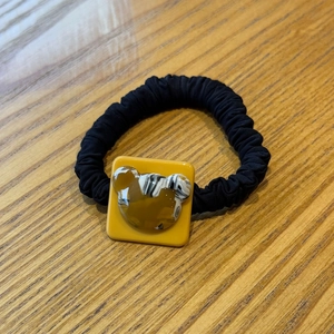 Close-up of black scrunchie hair tie with yellow resin bear charm on wood background