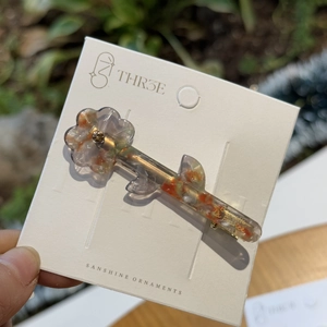 Detail of flower-shaped hair clip in orange and grey acetate on branded display card