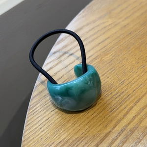 Dettaglio dell'elastico per capelli in resina marmorizzata verde con fascia nera su legno