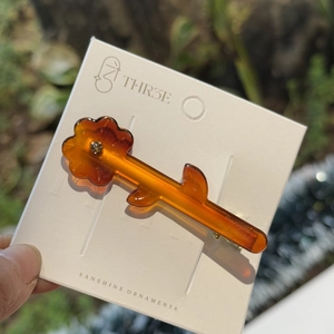 Macro detail of amber acetate flower hair clip with sparkling rhinestone center on card