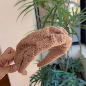 Detail van kameelbruine gebreide hoofdband met woltextuur en een gedraaide knoop