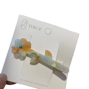 Floral acetate hair clip with marble pattern and blue rhinestone on white display card