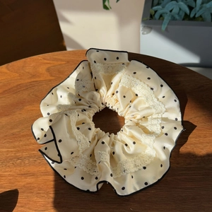 Polka dot satin scrunchie with lace trim and black piping on a wooden surface
