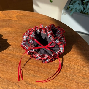 Detail of a red and green plaid drawstring pouch with ruffled edges and red satin bow