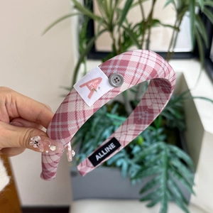 Detailaufnahme eines rosa karierten Stirnbandes mit Buchstaben-A-Aufnäher und Knopf