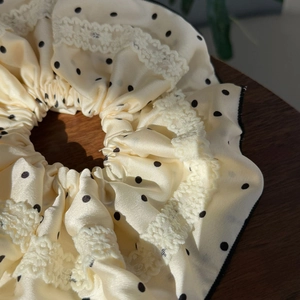 Detailed macro view of cream satin scrunchie with black polka dots and white lace edges