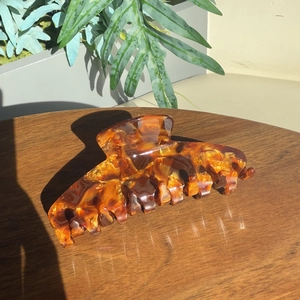 Pince à cheveux classique en acétate ambre sur table en bois avec ombre de plante