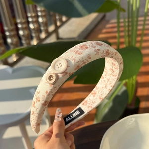 Détail du bandeau en lin floral avec boutons décoratifs et étiquette logo de la marque