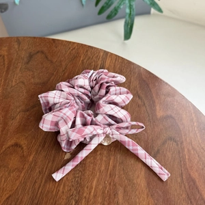 Detail eines rosa karierten Scrunchies mit Stoffschleife und gelbem Knopf auf Holz